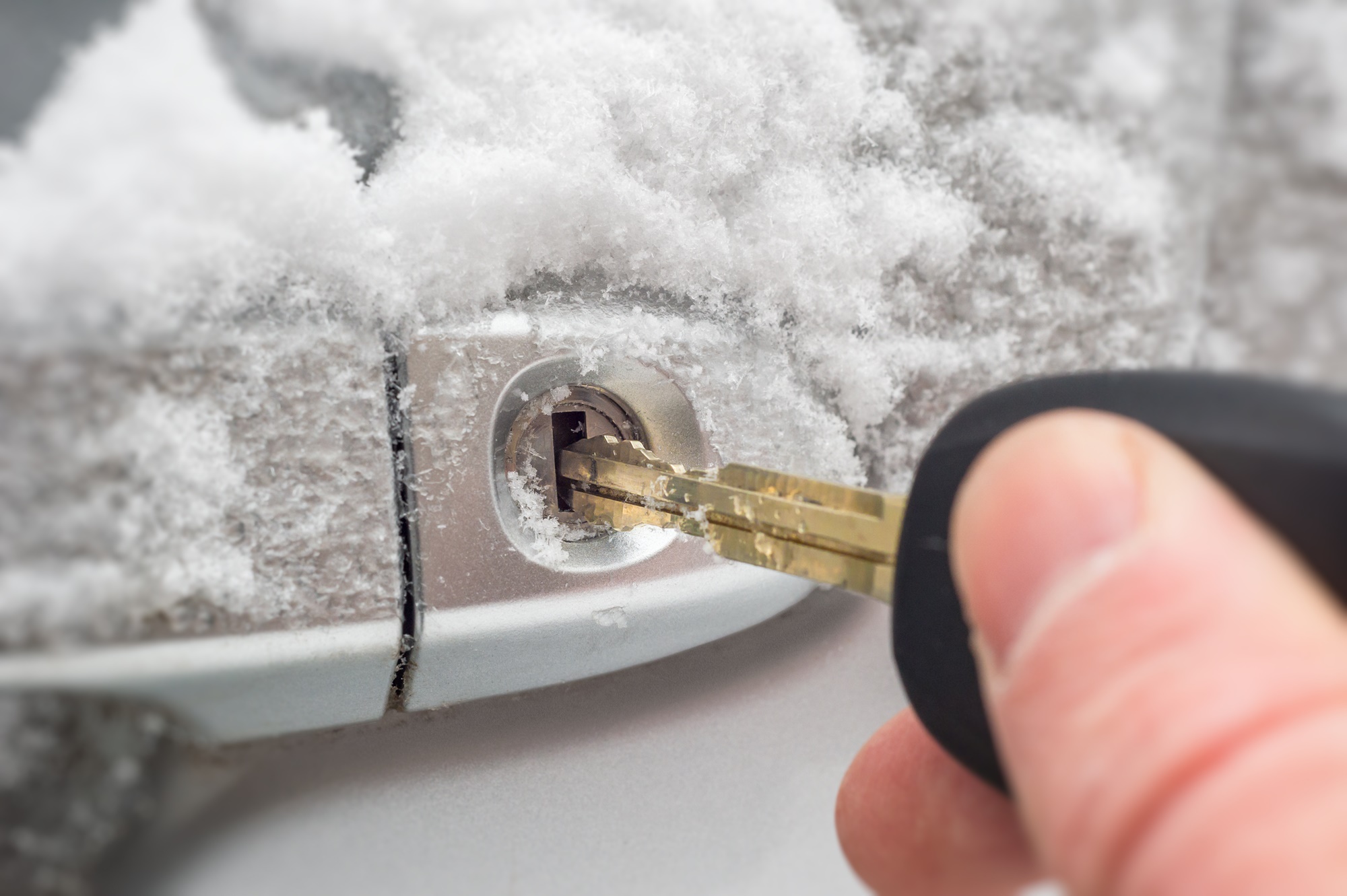 Osoba wsadzająca kluczyk do zamka w samochodzie pokrytego śniegiem.