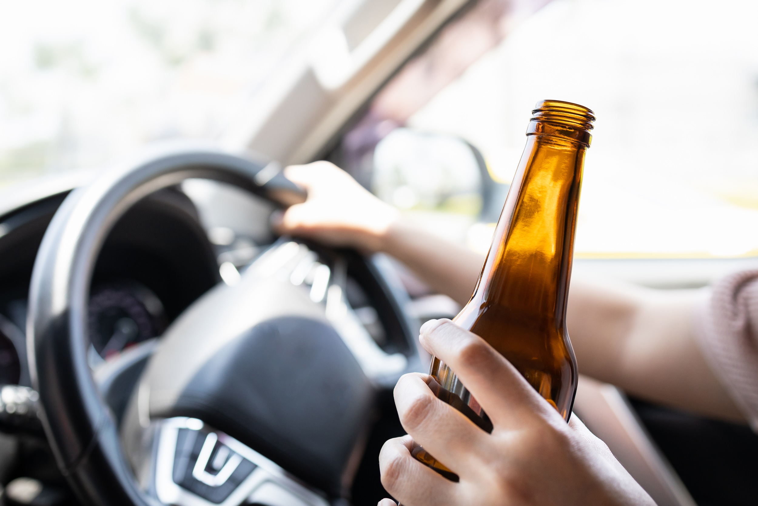 Osoba za kierownicą trzymająca w dłoni otwartą butelkę z alkoholem.