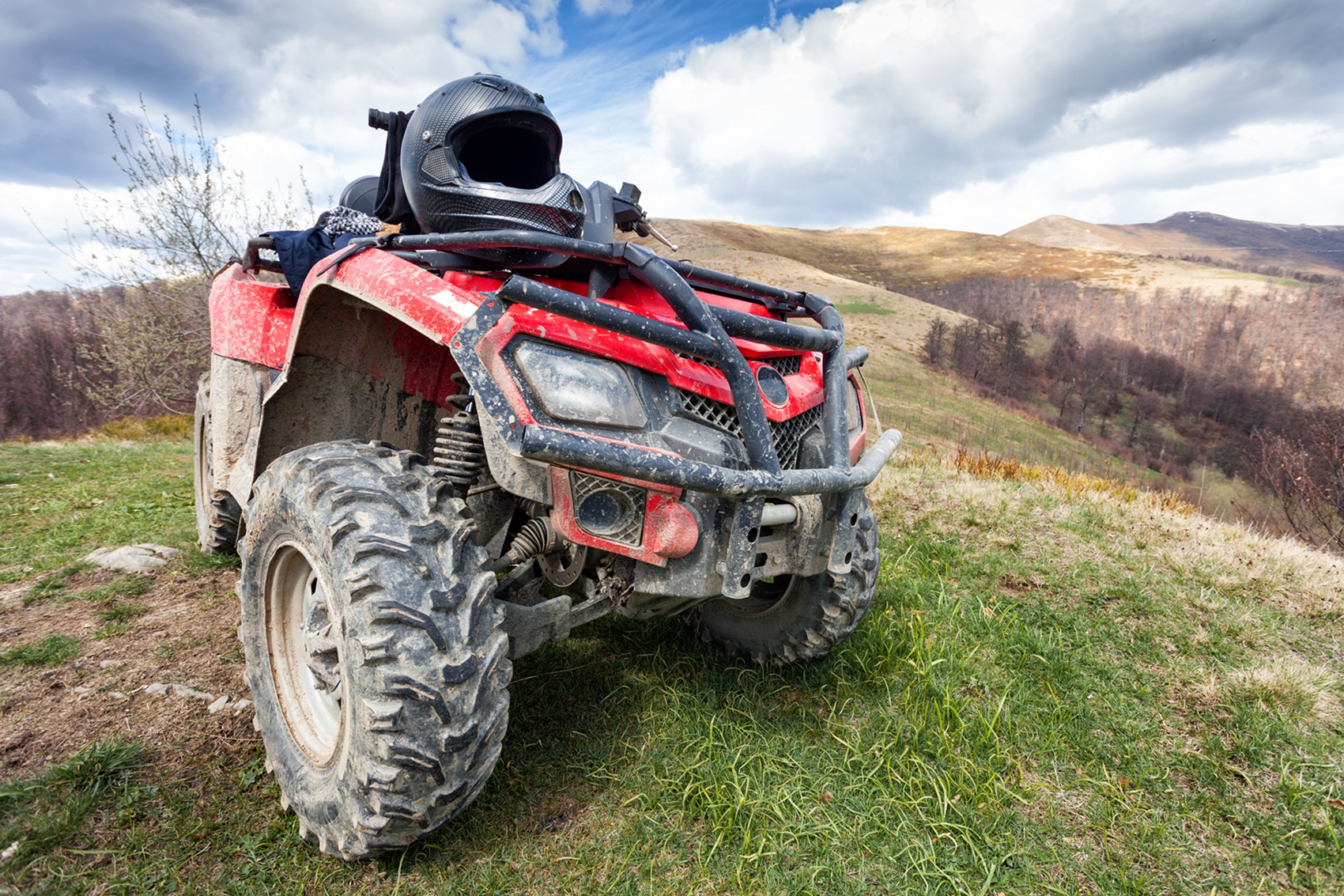 Czerwony quad w błocie stojący na zielonym wzgórzu