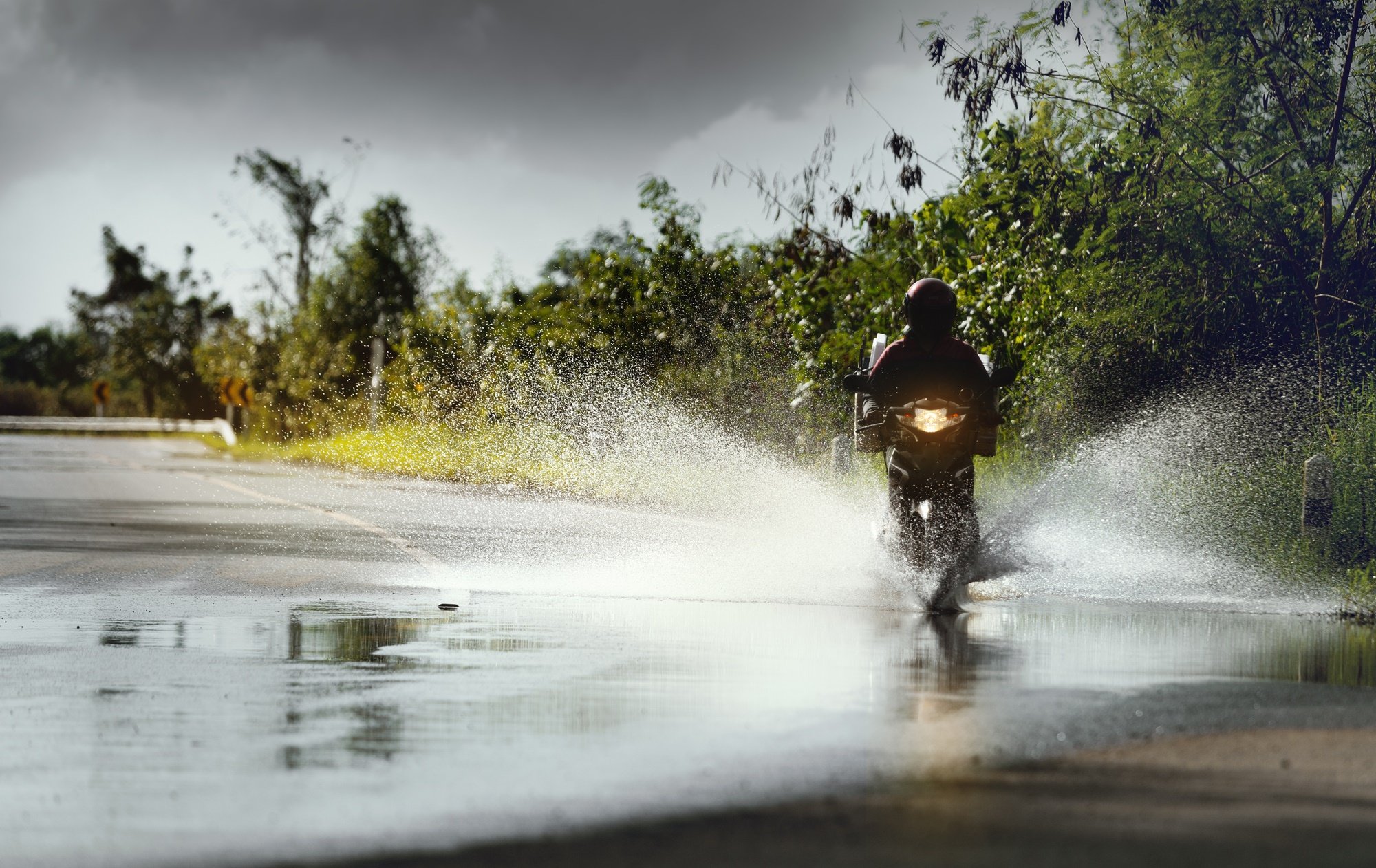 Motocyklista jadący motocyklem w deszcz po kałuży