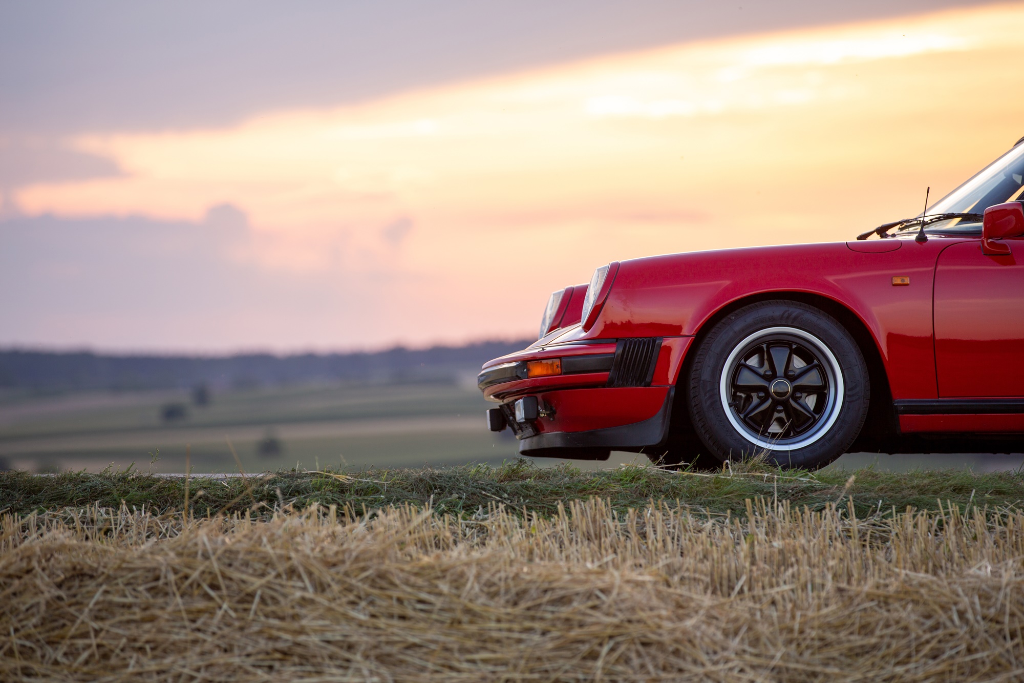 Przód czerwonego Porsche na tle łąk